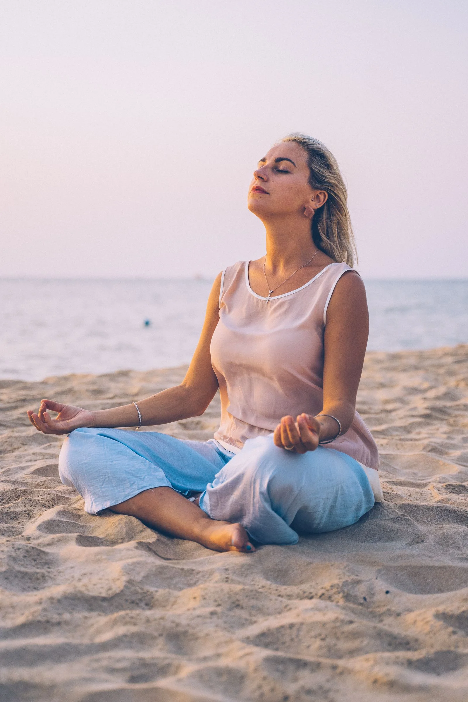Woman meditating on a beach at sunset