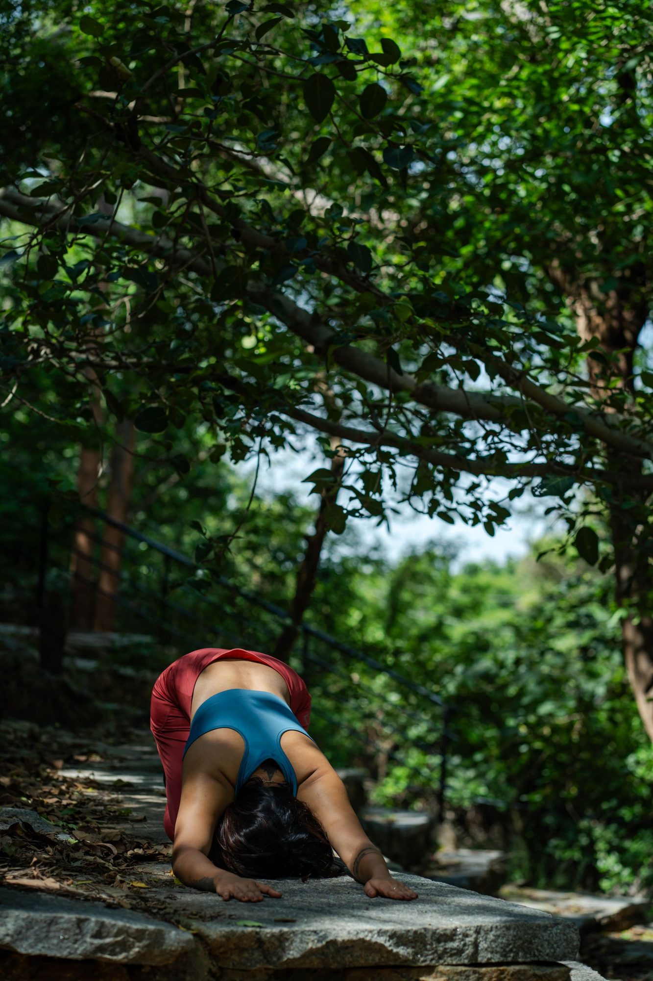 A woman practicing yoga on stone steps beneath leafy trees